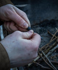 Hands holding a Ceramic Striker Ferro Rod Fire Starter Kit With Zirconia Stone For Emergency Survival by campfire, white