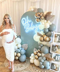 Neon Sign for Baby Shower Backdrop LED Light Up Wall Decor 21.5 Inch By 20 Inch Great for Gender Reveal Birthday Party Decorations Oh Baby Theme Great for Bedroom Walls and Photo Backdrops, displayed amidst balloons and cubes spelling 'BABY' with a pregnant woman posing.