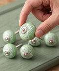Hand holding a Top Shelf Vintage Floral Ceramic Cabinet Knob, 40mm round green design from the six-piece set for easy furniture upgrades.