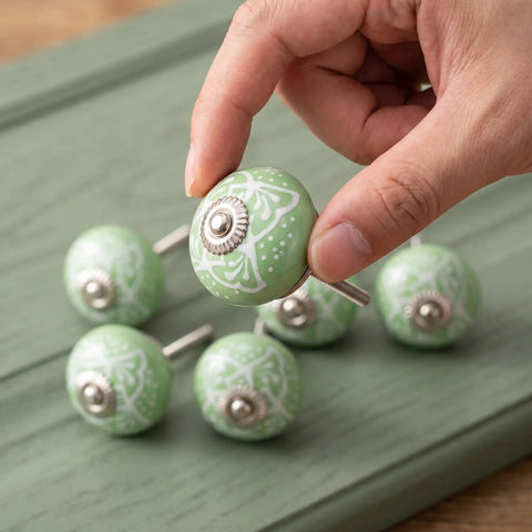 Hand holding a Top Shelf Vintage Floral Ceramic Cabinet Knob, 40mm round green design from the six-piece set for easy furniture upgrades.