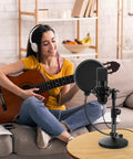 Woman playing guitar next to a multifunctional desktop microphone stand for live streaming and studio recording with pop filter