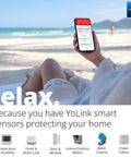 Person holding smartphone showing real-time app alerts for smart wireless temperature and humidity sensor on a beach.