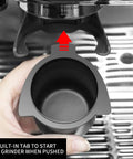 Hand holding 54mm Espresso Dosing Cup for Portafilter with Grinder Activating Ring Matte Black grounds cup under grinder.