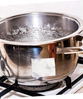 Stainless steel pot with water boiling on a gas stove in a kitchen setting.