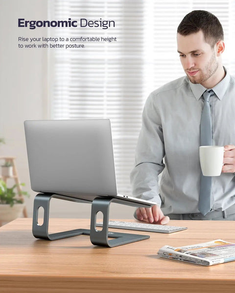 All Aluminum Laptop Stand For Desk Setup With Ventilated Cooling Detachable Ergonomic Riser Anti Slip Notebook Holder For 10-16 Inch Laptops Like MacBook, Dell XPS, HP, Lenovo And ThinkPad on a desk with a person in the background