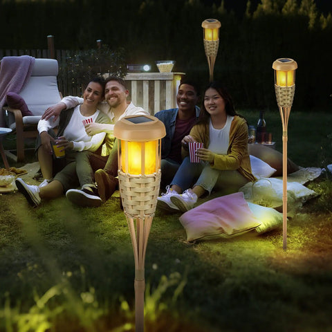 Group enjoying a cozy nighttime setting with Solar Torch Lights With Realistic Flickering Flame Outdoor Yard Path And Patio Decor 4 Pack Waterproof LED Garden Lights With Bamboo Weave For Easy Install Cozy Night Vibe And Dope Nighttime Ambiance illuminating the garden.