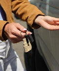 Straight Up Solid Car Escape Keychain With Seatbelt Cutter And Tempered Glass Window Breaker Made In Usa held by a person near a vehicle.