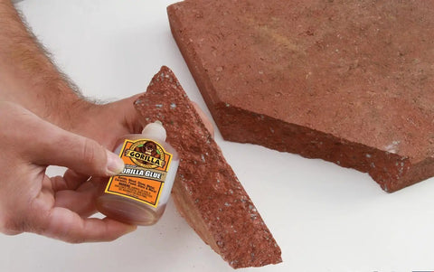 Waterproof Polyurethane Glue For Wood Stone Metal Heavy Duty Adhesive applied on a piece of red stone, hand holding bottle