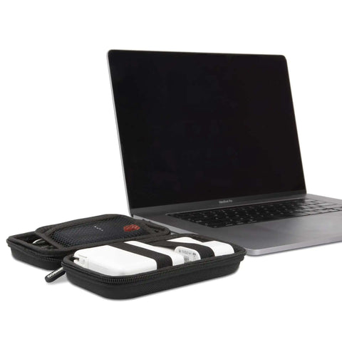 Hard Shell Tech Travel Case With All In One Cable Organizer And Mesh Pockets for adapters next to a MacBook Pro.