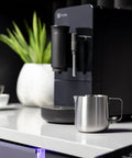 Game Changer Automatic Espresso Machine Packing Built In Milk Frother on kitchen counter with stainless steel milk frothing pitcher.