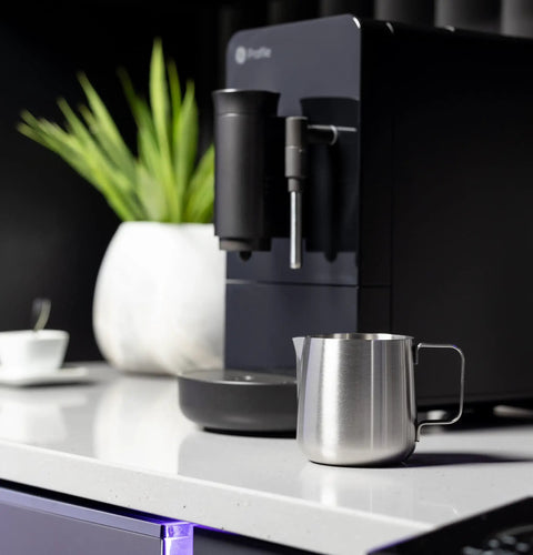 Game Changer Automatic Espresso Machine Packing Built In Milk Frother on kitchen counter with stainless steel milk frothing pitcher.