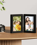 Double 4x6 Picture Frame Vertical From Engineered Wood With Plexiglass Bifold Photo Frame For Tabletop Display Holds Two 4x6 Photos In A Dope Black Finish That Fits Any Desk Or Shelf on wooden table with a camera.