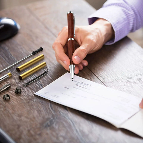 Slimline Pen Kit Set 30 Wood Turning Twist Pen Kits With Refills shown in a hand writing on paper, with gold and silver tubes