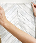 Hands applying White And Tan Herringbone Wood Look Peel And Stick Wallpaper For Renters And Homeowners, Removable Vinyl