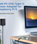 Beefy GaN 27W USB C PD Power Adapter For Raspberry Pi 5 Five Point One Volt Five Amp Charger With 130 Centimeter Cable And 100 240V AC Input Built To Power Pi 5 And Peripherals Across 16GB 8GB 4GB And 2GB RAM Models, shown installed on a wall near a desk with Raspberry Pi