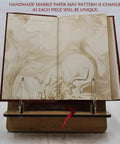 Open marble-patterned page in 'From Raw Wool To Finished Goods: A Rugged Premium Leather Bound Guide To Wool Crafting, 186 Page Collector’s Edition, English, By Hunter J A, Released 2024' displayed on a wooden stand.