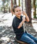 Child on Heavy Duty Wooden Zip Line Seat For Backyard Adventures, Pine Wood Frame Holds Up To 350 Lbs, in forest setting.