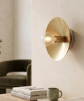 NautiGlow Modern Brass Brushed Wall Sconce with Round Backplate, Exposed Globe Light Fixture on wall beside a chair.