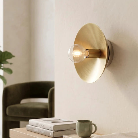 NautiGlow Modern Brass Brushed Wall Sconce with Round Backplate, Exposed Globe Light Fixture on wall beside a chair.