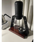 Straight Up Solid Coffee Stand And Dripper Holder Built With Heavy Duty Carbon Steel And Wooden Pedestal Base For Clean Manual Brew Organization That Stays Crisp, featuring a glass server, metal cup, and brewing station.