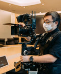Person using Thanos Pro Gimbal Vest Stabilizer System with Adapter Arm for filming in an office, shifting weight from hands to waist.