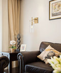 Set of 2 Gold Wall Sconces With Clear Glass Shade in living room, gold finish metal mount on wall above leather armchair