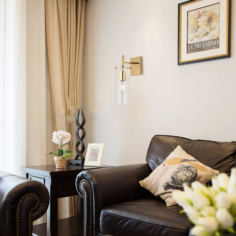 Set of 2 Gold Wall Sconces With Clear Glass Shade in living room, gold finish metal mount on wall above leather armchair