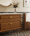 Wooden bathroom vanity with gold sunburst cabinet handles, decorative tile backsplash, and a countertop displaying floral decor.