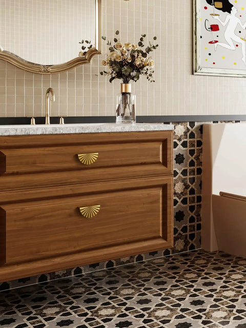 Wooden bathroom vanity with gold sunburst cabinet handles, decorative tile backsplash, and a countertop displaying floral decor.