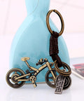 Vintage Leather And Bronze Bicycle Keychain With Metal Wheel And Handlebars Pendant against a blue vase background