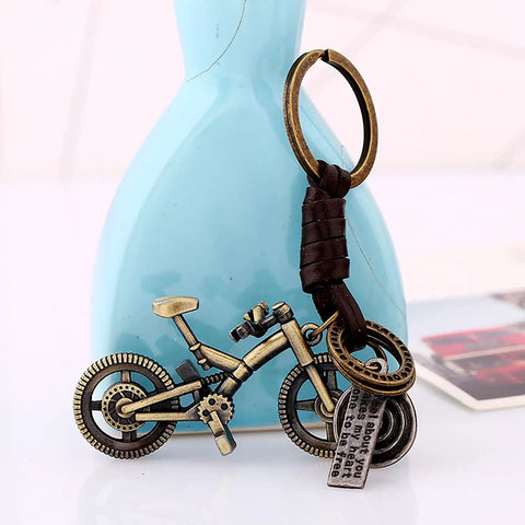 Vintage Leather And Bronze Bicycle Keychain With Metal Wheel And Handlebars Pendant against a blue vase background