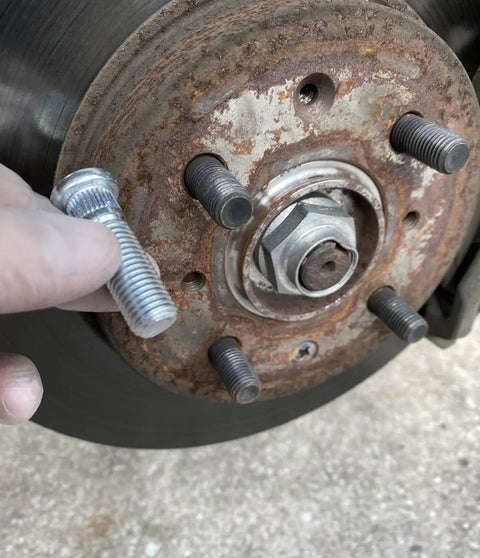 Close-up of wheel hub with hand inserting a lug bolt, part of 10Pcs M12x1.5 Wheel Studs 43mm Lug Bolts For Honda Accord Civic CRV CRX.