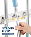 Close-up of Over The Door Broom And Mop Holder With 4 Slots And 4 Hooks, showing strong grip with hand placing a mop.