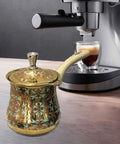 Decorative Turkish Coffee Pot in front of an espresso machine, highlighting its functionality next to modern appliances.