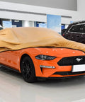 Orange Ford Mustang covered by Tough As Nails Heavy Duty Outdoor Car Cover For Ford Mustang 1994 Through 2026 in a showroom