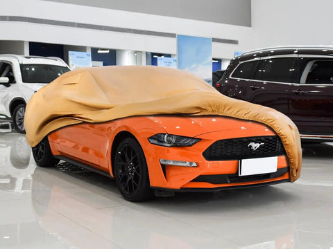 Orange Ford Mustang covered by Tough As Nails Heavy Duty Outdoor Car Cover For Ford Mustang 1994 Through 2026 in a showroom