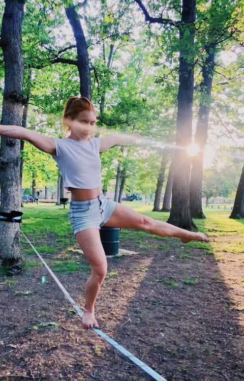 Person balancing on 60 Feet Slackline Kit With Tree Guards, Carry Bag, And Easy Setup for Family Fun in a park