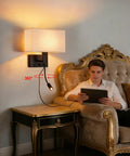 Hardwired Black Wall Sconce With USB Port And Reading Lamp next to a man on a sofa, features linen shade, modern design, dual switches