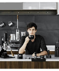 Level Up Your Home Barista Setup With This Dope 58Mm Espresso WDT Tool Featuring Six Heat Resistant Needles Adjustable Depth Control And Hidden Magnetic Storage For Zero Fuss Morning Routines, showing a barista holding a black cup.