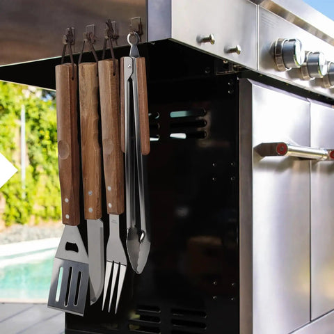 Stainless Steel BBQ Grill Tools Set with ergonomic wood handles hung on a grill, includes spatula, tongs, knife, and fork for outdoor grilling.