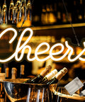 Cheers neon sign with USB and battery power on bar setup, warm white LED glow, for parties and celebrations.