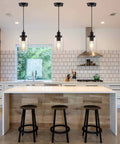 Three Pack Black Industrial Pendant Lights With Clear Glass Shades hanging over a modern kitchen island with wooden stools.