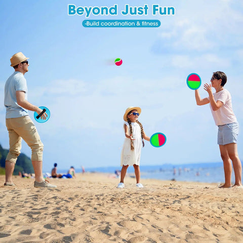 Family playing with Toss And Catch Ball Set For Kids Outdoor Yard Games Beach Toy with 4 paddles and 4 balls on a sunny beach.