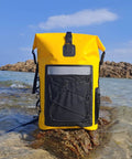 Yellow waterproof roll-top backpack with padded straps 35L daypack for hiking and camping on a rocky shore