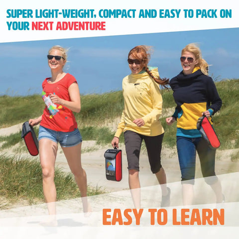 Three women holding beach kite bags, walking on grass with clear skies.