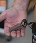 Close-up of a hand holding a steel clip with a strap, used with Tough As Nails Beefed Up Steel Toe Rubber Boots With Snake Proof Hip Waders.