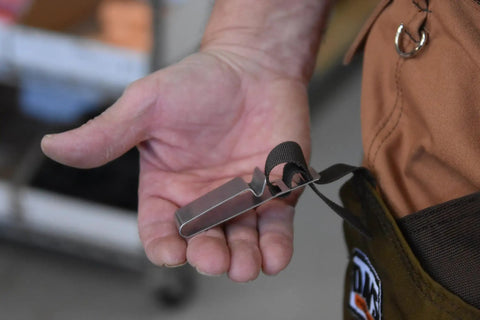 Close-up of a hand holding a steel clip with a strap, used with Tough As Nails Beefed Up Steel Toe Rubber Boots With Snake Proof Hip Waders.
