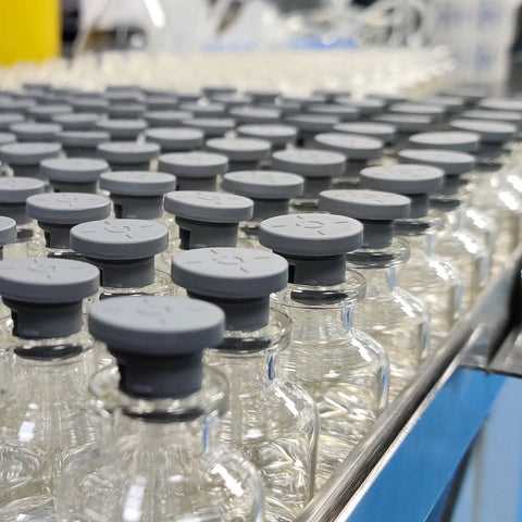 Glass vials with grey rubber stoppers on a production line