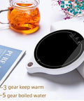 Solid Pick Mug Warmer And 200W Cup Heater That Keeps Your Daily Grind Steaming Hot Up To 100C With Five Precise Temperature Levels Plus Non Slip Base For Desk placed next to a glass tea pot and book.