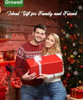 Couple holding a red gift box beside a Christmas tree, wearing festive sweaters, with decorated room in the background.